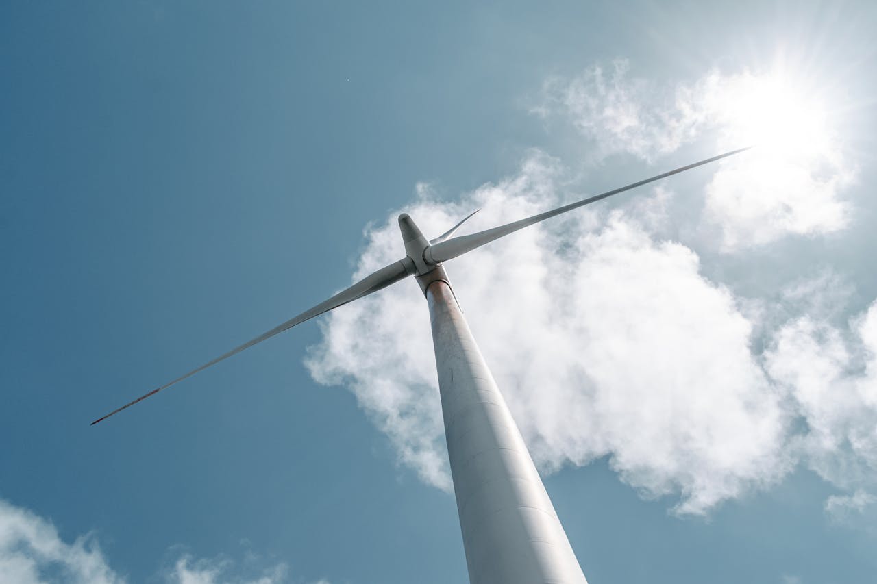 Low-angle view of a wind turbine with sunlight and clouds in the sky.